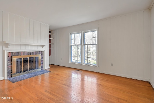 unfurnished living room with light hardwood / wood-style floors, a fireplace, and wooden walls