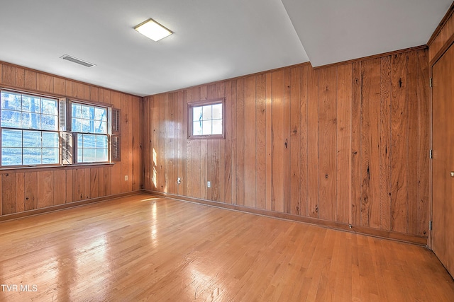 unfurnished room with wooden walls, light hardwood / wood-style floors, and a healthy amount of sunlight