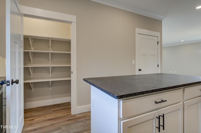 kitchen with white cabinets, light hardwood / wood-style flooring, ornamental molding, and dark stone countertops