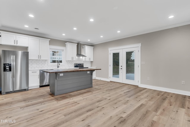 kitchen featuring a center island, white cabinets, wall chimney range hood, light wood-type flooring, and stainless steel appliances