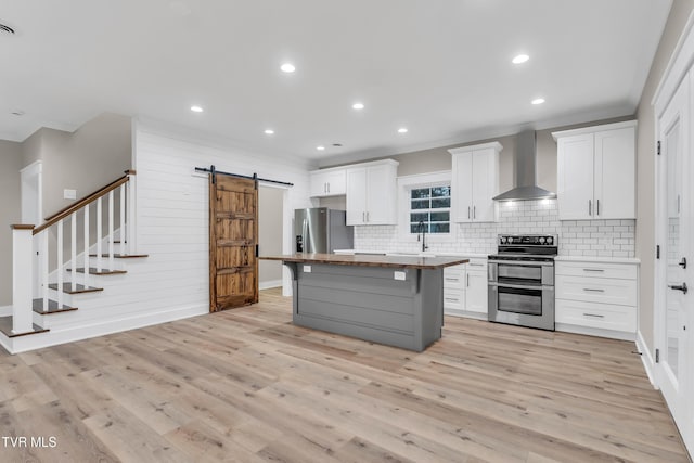 kitchen featuring wall chimney range hood, a barn door, light hardwood / wood-style floors, a kitchen island, and appliances with stainless steel finishes