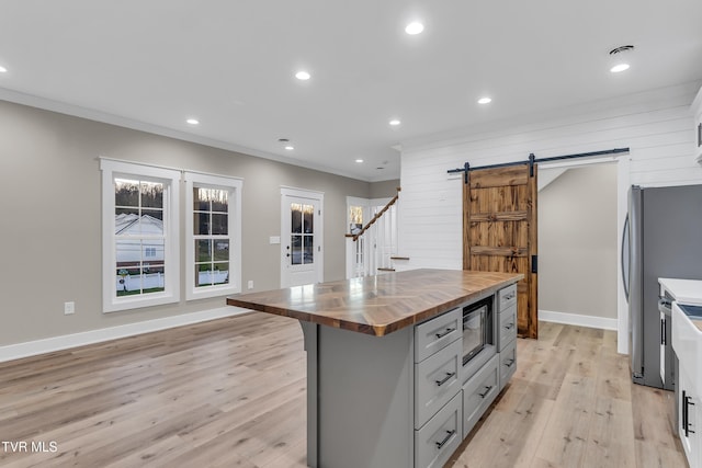 kitchen with light wood-type flooring, a barn door, gray cabinets, a center island, and butcher block countertops