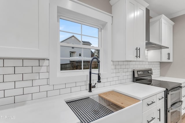 kitchen featuring wall chimney exhaust hood, white cabinetry, electric stove, and sink