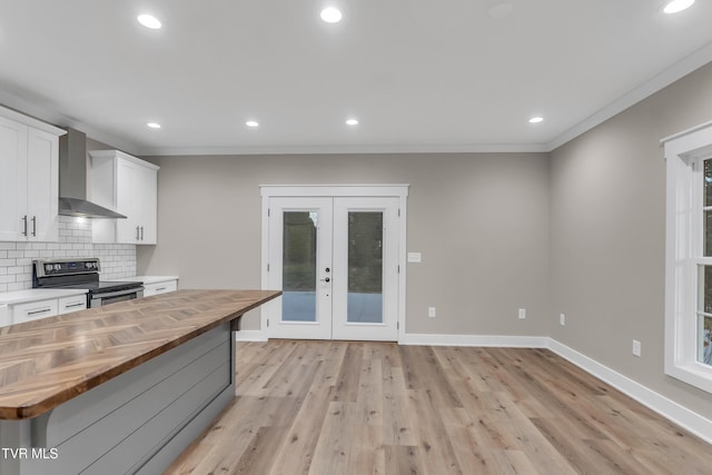 kitchen with white cabinetry, french doors, wall chimney range hood, butcher block countertops, and stainless steel electric range