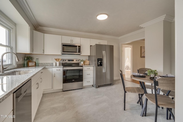 kitchen featuring white cabinets, appliances with stainless steel finishes, light stone countertops, crown molding, and a sink