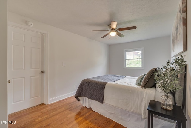 bedroom featuring a textured ceiling, ceiling fan, light wood-type flooring, and baseboards