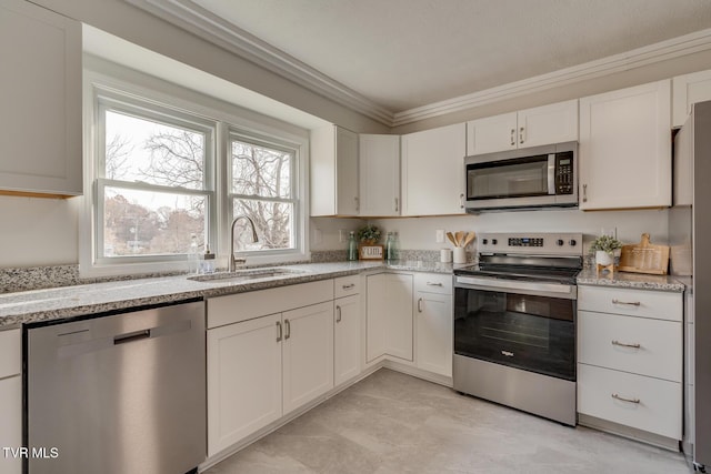 kitchen with white cabinets, light stone counters, appliances with stainless steel finishes, crown molding, and a sink