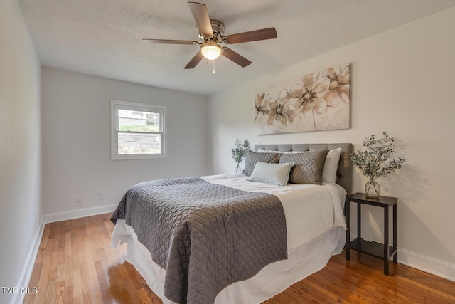 bedroom with a ceiling fan, a textured ceiling, baseboards, and wood finished floors