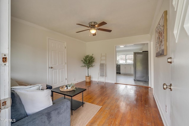 living area with a ceiling fan, crown molding, baseboards, and wood finished floors