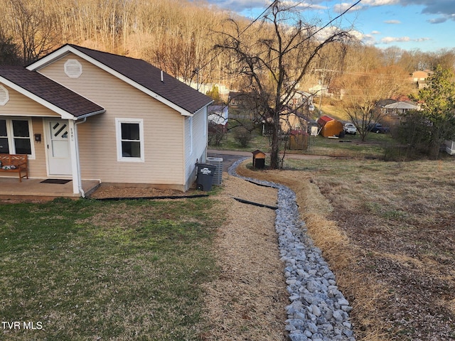 view of side of home featuring roof with shingles and a yard