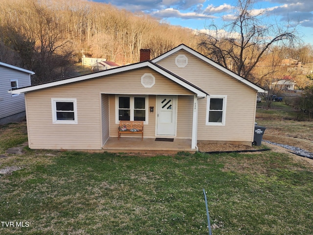 view of front facade with a front yard, covered porch, and a chimney