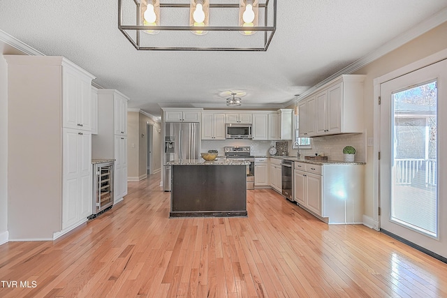 kitchen with ornamental molding, stainless steel appliances, a center island, light hardwood / wood-style floors, and white cabinetry