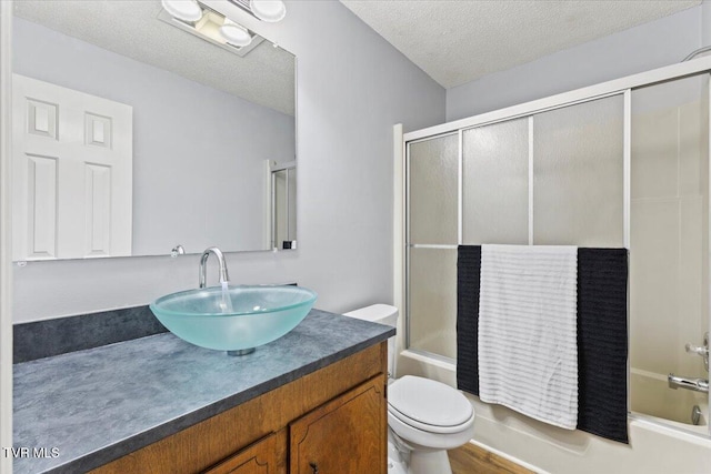 full bathroom with vanity, a textured ceiling, hardwood / wood-style flooring, enclosed tub / shower combo, and toilet