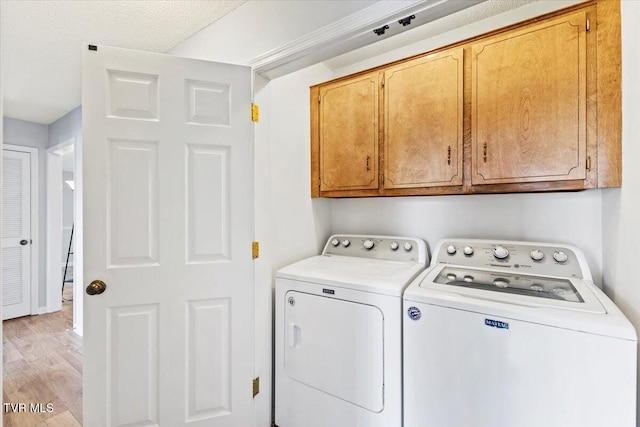 laundry room featuring washer and clothes dryer, cabinets, light wood-type flooring, and a textured ceiling