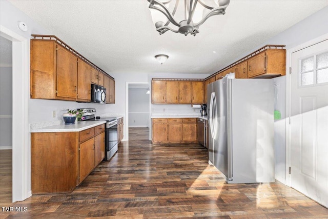 kitchen with a textured ceiling, stainless steel appliances, an inviting chandelier, and dark wood-type flooring