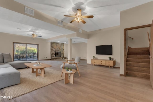 living room with a stone fireplace, ceiling fan, and light hardwood / wood-style floors