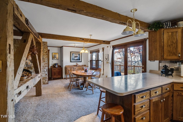 kitchen featuring a kitchen bar, decorative light fixtures, beam ceiling, light colored carpet, and kitchen peninsula