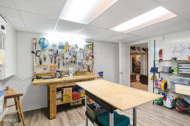 basement featuring a workshop area, a drop ceiling, and wood-type flooring