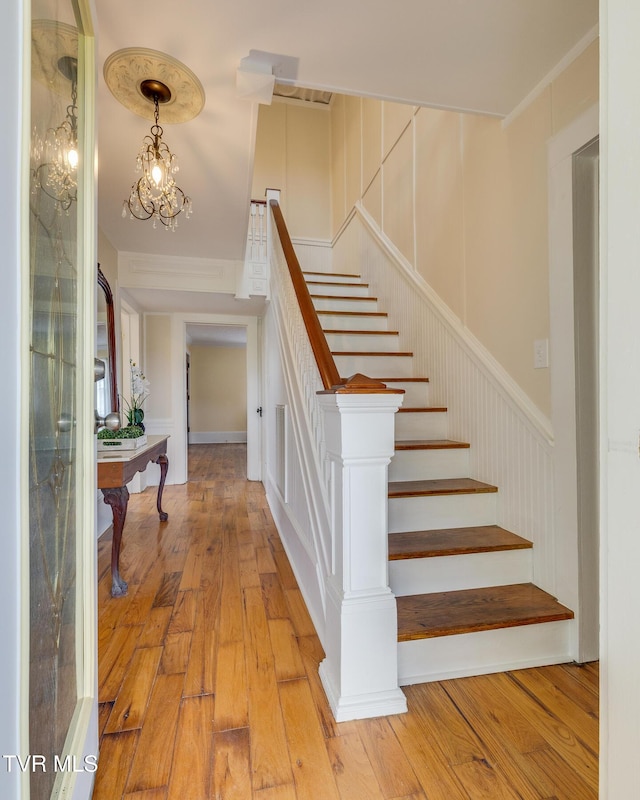 stairs with crown molding, a notable chandelier, and hardwood / wood-style flooring