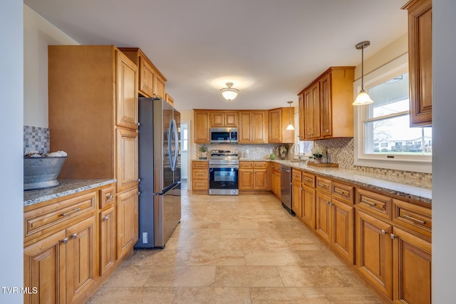 kitchen featuring light stone countertops, stainless steel appliances, hanging light fixtures, and sink