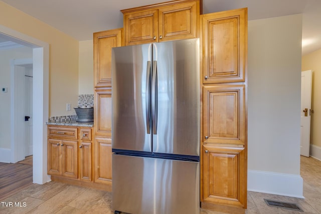 kitchen featuring decorative backsplash, stainless steel fridge, light stone counters, and light wood-type flooring