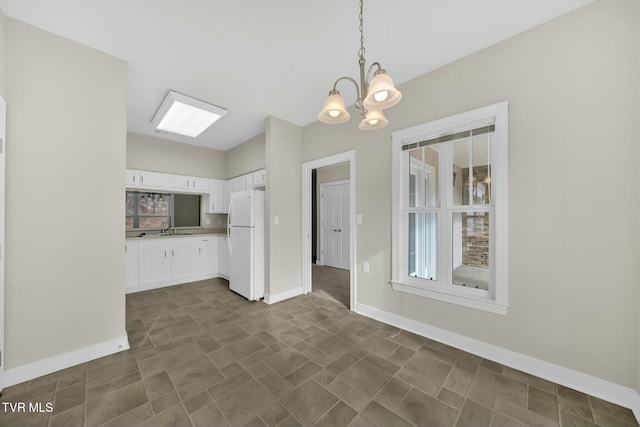 kitchen featuring an inviting chandelier, sink, hanging light fixtures, white fridge, and white cabinetry