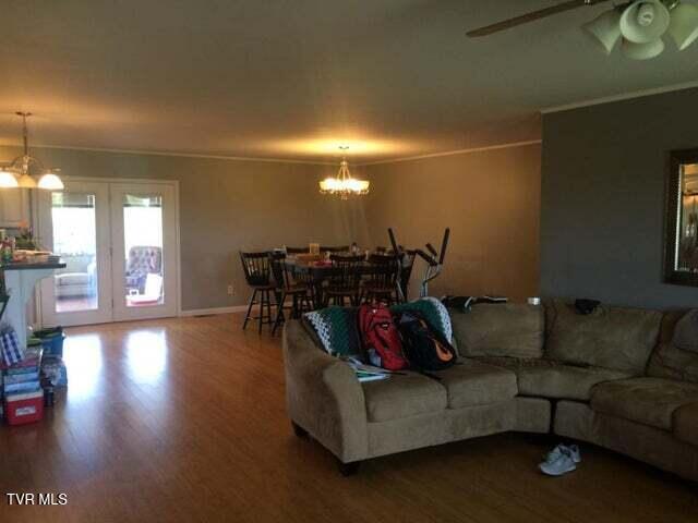 living room with ceiling fan with notable chandelier, wood-type flooring, crown molding, and french doors