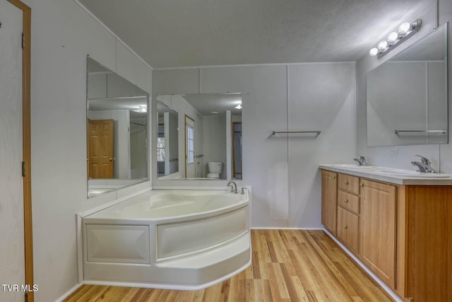 bathroom featuring a bathing tub, a textured ceiling, toilet, vanity, and hardwood / wood-style flooring