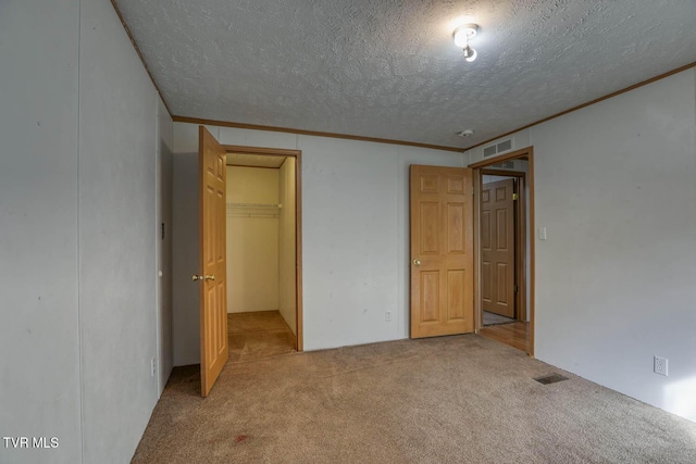 unfurnished bedroom with light carpet, a textured ceiling, a closet, and a walk in closet