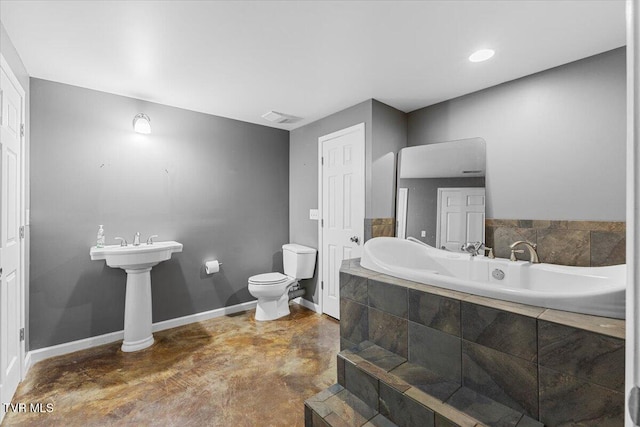 bathroom with a relaxing tiled tub, concrete floors, and toilet