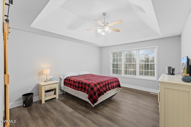 bedroom featuring ceiling fan, dark wood-type flooring, and a tray ceiling