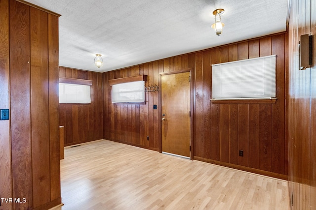 empty room with wood walls, light hardwood / wood-style flooring, and a textured ceiling