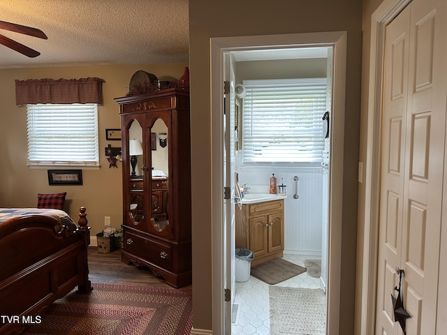 bedroom with ceiling fan, sink, a textured ceiling, and ensuite bath