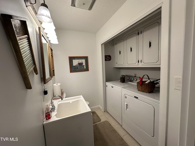 clothes washing area with sink, cabinets, a textured ceiling, washer and clothes dryer, and light tile patterned flooring