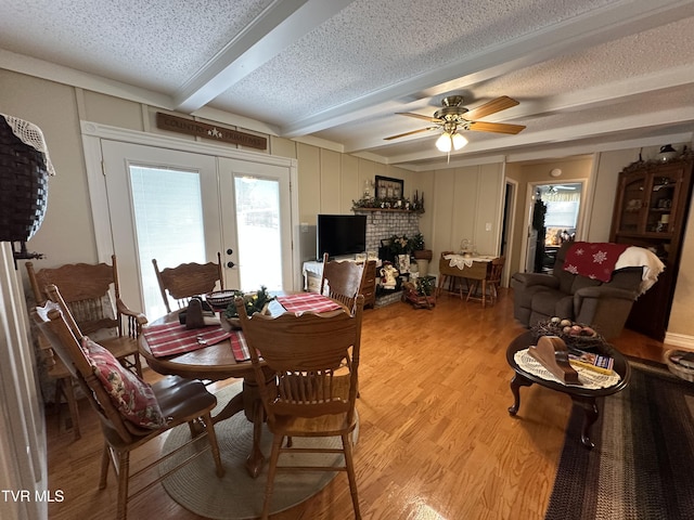 dining area with french doors, ceiling fan, light wood-type flooring, a textured ceiling, and beamed ceiling