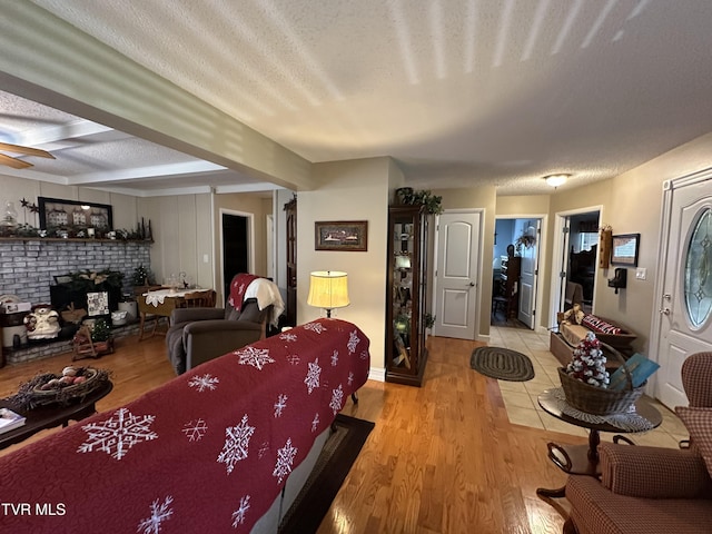 living room featuring ceiling fan, light wood-type flooring, a textured ceiling, and a brick fireplace