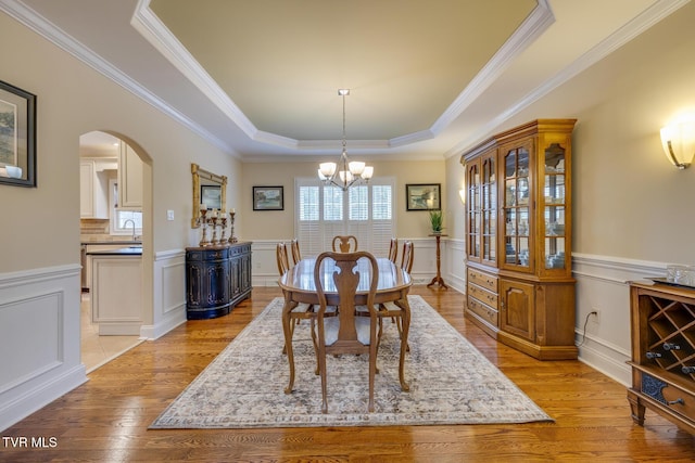 dining room featuring light wood-type flooring, a raised ceiling, and crown molding