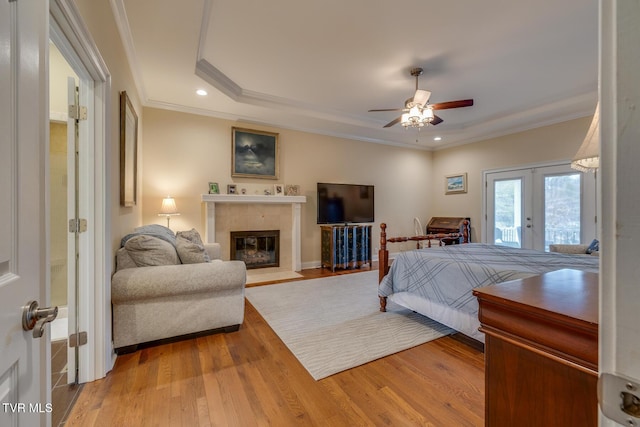 bedroom with french doors, ornamental molding, ceiling fan, a tile fireplace, and wood-type flooring