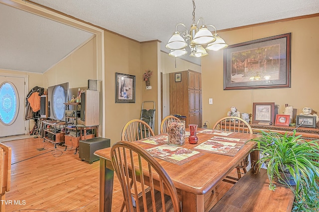 dining area with a textured ceiling, light wood-type flooring, an inviting chandelier, and lofted ceiling