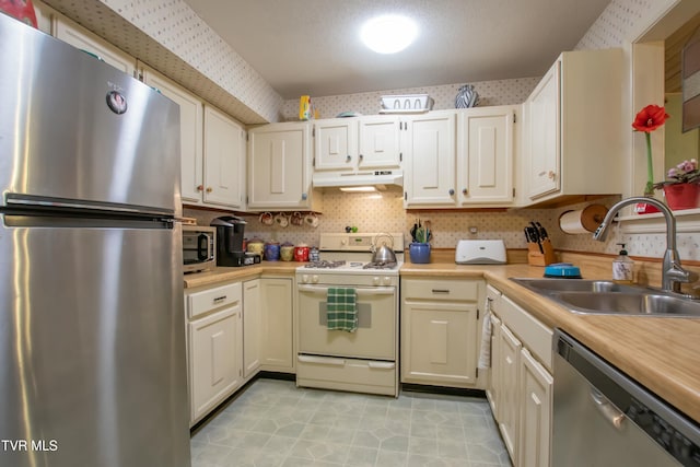 kitchen with sink, tasteful backsplash, a textured ceiling, light tile patterned floors, and appliances with stainless steel finishes