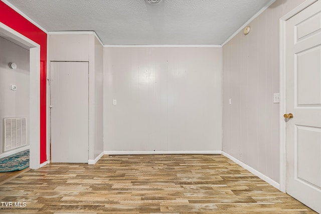 empty room with light hardwood / wood-style floors, ornamental molding, and wooden walls