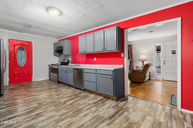 kitchen with appliances with stainless steel finishes, light wood-type flooring, ornamental molding, a textured ceiling, and sink