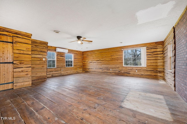 unfurnished living room with rustic walls, a wall mounted AC, dark wood-type flooring, and ceiling fan