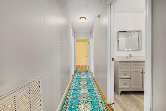 hallway with sink, light wood-type flooring, and a textured ceiling