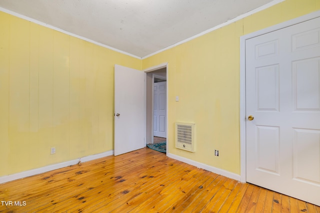 empty room with heating unit, crown molding, and wood-type flooring