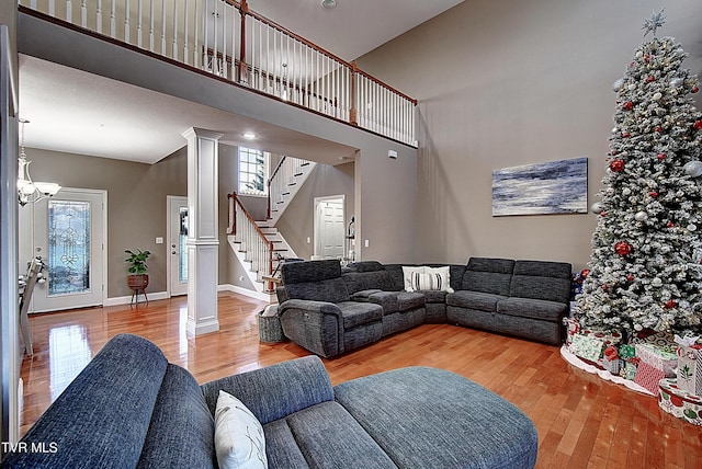 living room featuring a towering ceiling, light wood-type flooring, decorative columns, and a notable chandelier