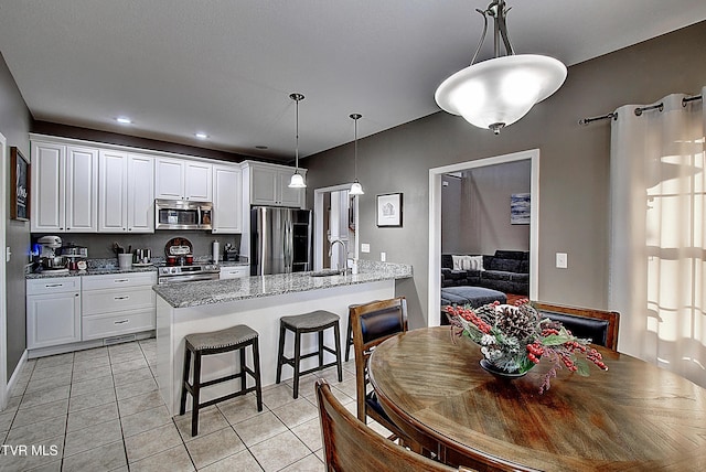 kitchen with decorative light fixtures, light stone counters, white cabinetry, and stainless steel appliances