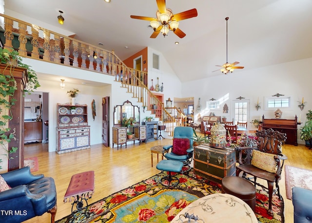 living area featuring stairs, high vaulted ceiling, wood finished floors, and a ceiling fan