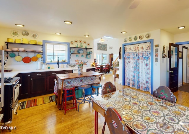 kitchen featuring light wood finished floors, gas range oven, open shelves, and light countertops