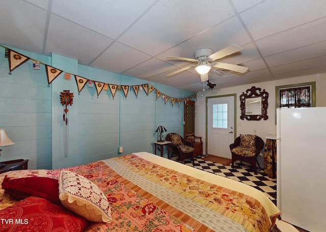 bedroom with ceiling fan, a paneled ceiling, and concrete block wall